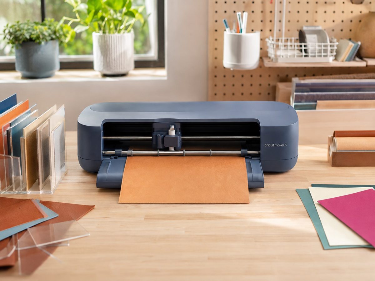 Slate Blue Cricut Maker 5 feeding leather in a bright craft studio, shown as an editorial illustration